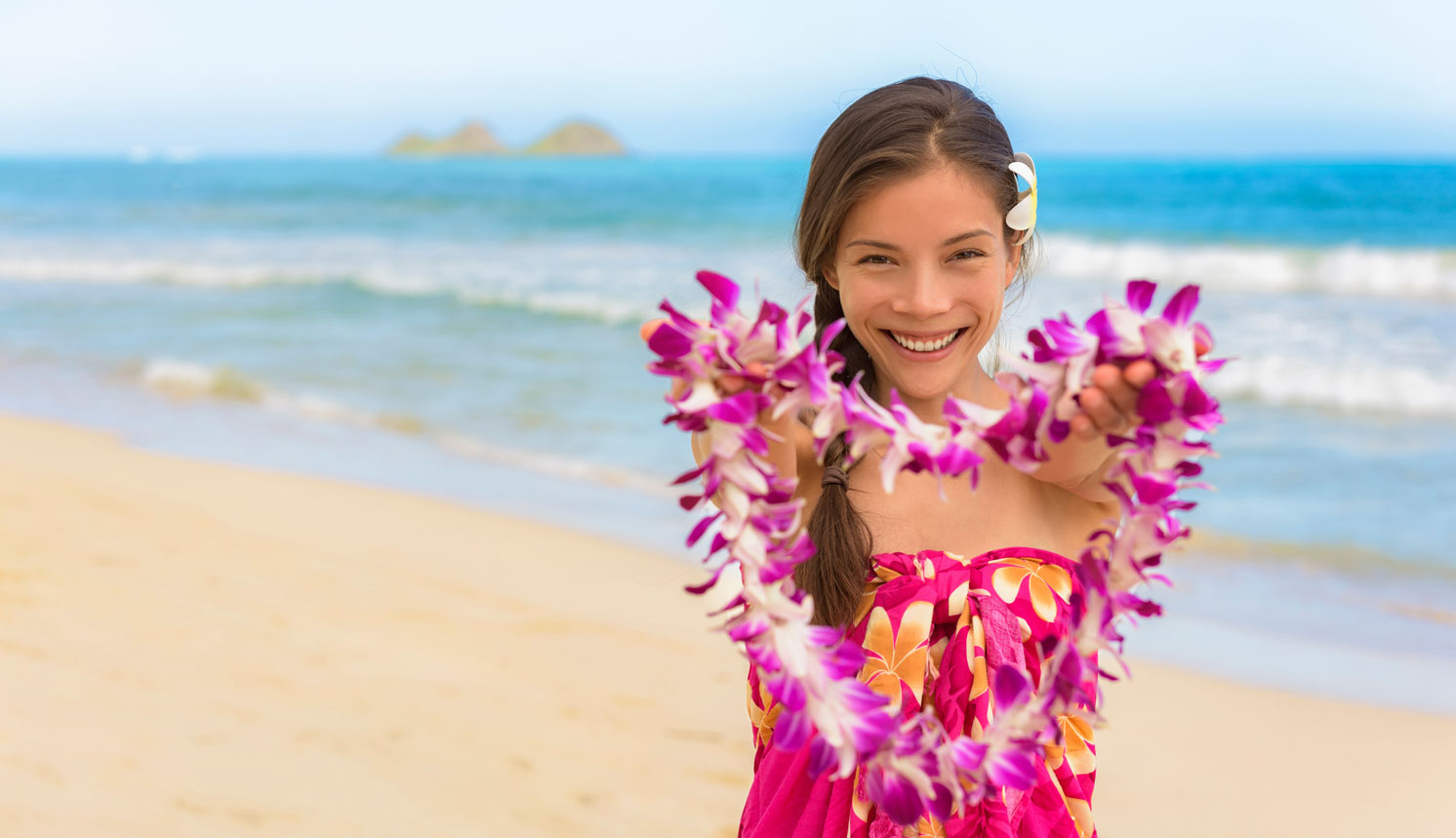 Leilani welcoming you on a sunny Hawaiʻi beach, holding a lei.